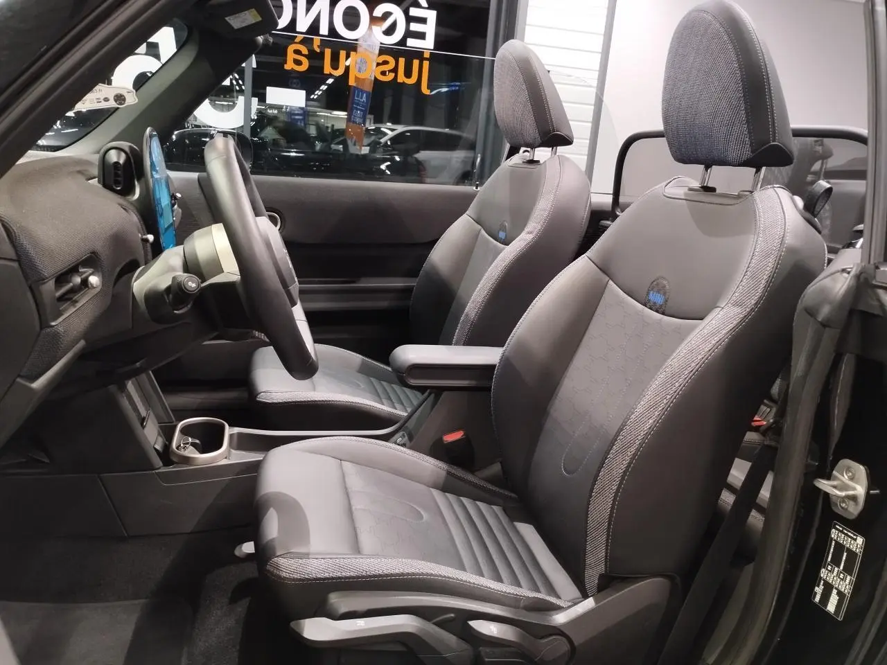 Vue intérieure côté conducteur du cabriolet MINI noir 2025 avec sièges sport en similicuir perforé noir et accoudoir central.