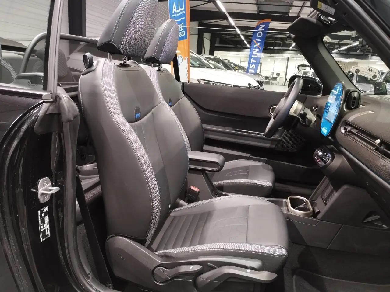 Vue intérieure côté gauche du cabriolet MINI noir, mettant en valeur les sièges sport en similicuir perforé avec accoudoir central.