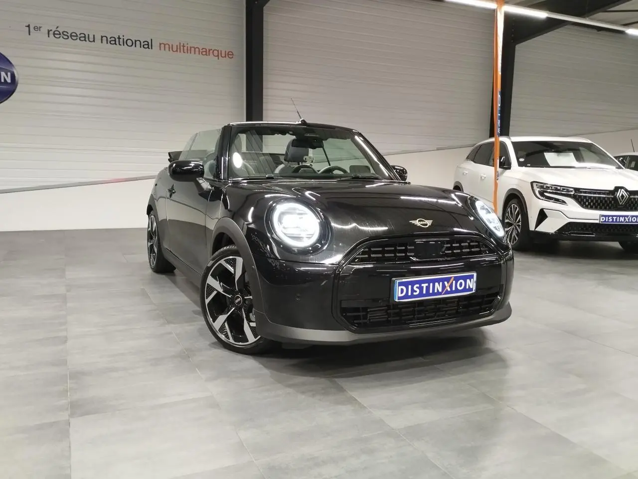 MINI Cabriolet noir vue 3/4 avant droit en intérieur, avec jantes noires à motifs et capote ouverte.