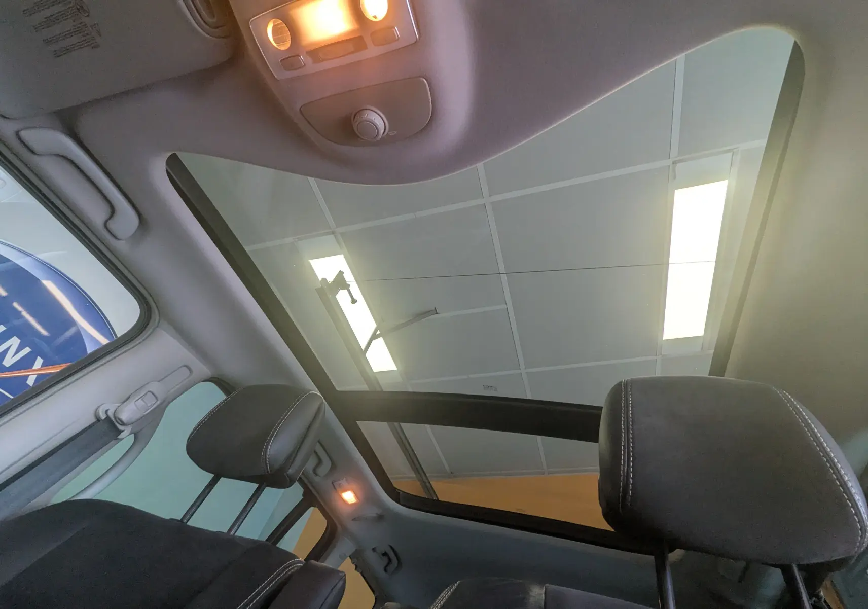 Vue intérieure du toit panoramique et des appuie-têtes noirs du Renault Grand Espace IV gris clair, éclairage intérieur allumé.