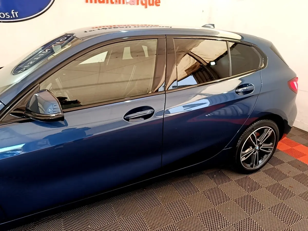 Vue latérale gauche d'une BMW Série 1 118i Edition Sport bleu avec jantes alliage et rétroviseurs ton caisse.