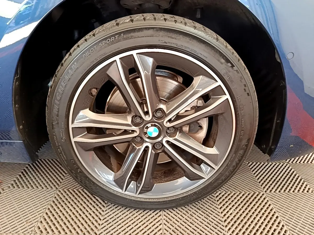 Gros plan sur la roue avant droite avec jante alliage BMW et carrosserie bleu de la Série 1 118i Edition Sport.