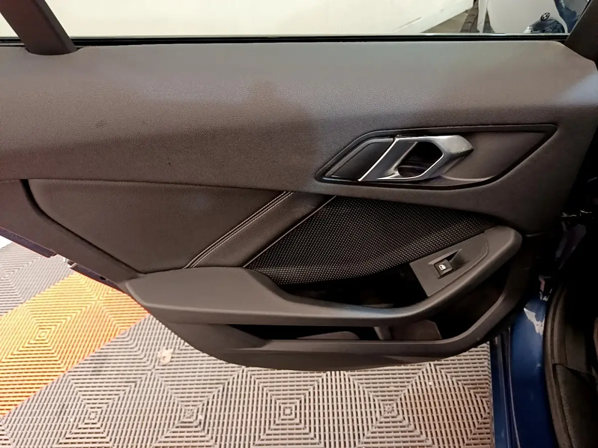 Gros plan sur la porte intérieure côté gauche d'une BMW Série 1 118i Edition Sport bleu, avec poignée et commande de vitre.