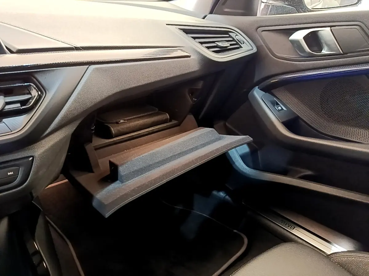 Intérieur BMW Série 1 118i Edition Sport 2023, vue côté passager sur boîte à gants ouverte et tableau de bord noir.