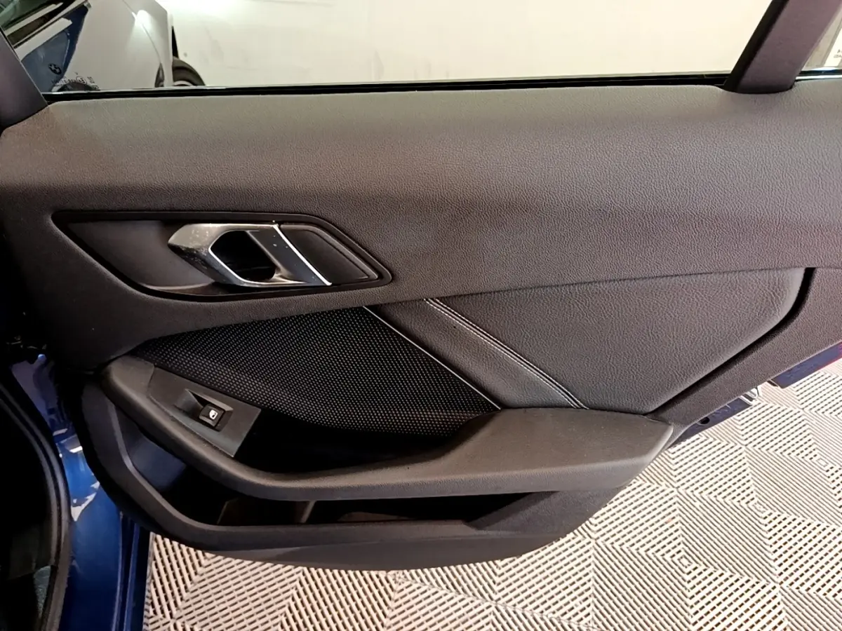 Vue rapprochée de la porte côté gauche bleu de la BMW Série 1 118i Edition Sport avec poignée et bouton de vitre électrique.