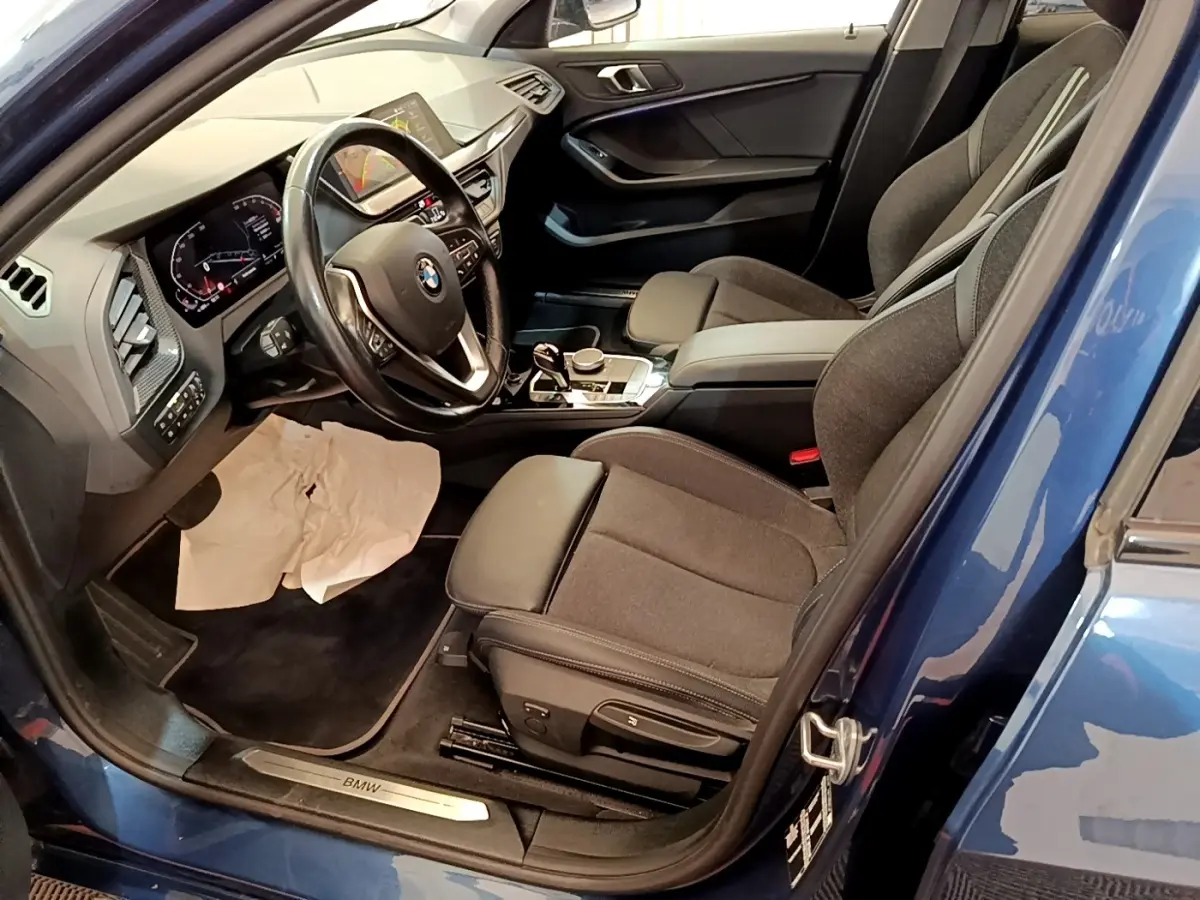 Vue intérieure côté conducteur de la BMW Série 1 118i Edition Sport bleue, avec tableau de bord et sièges noirs.