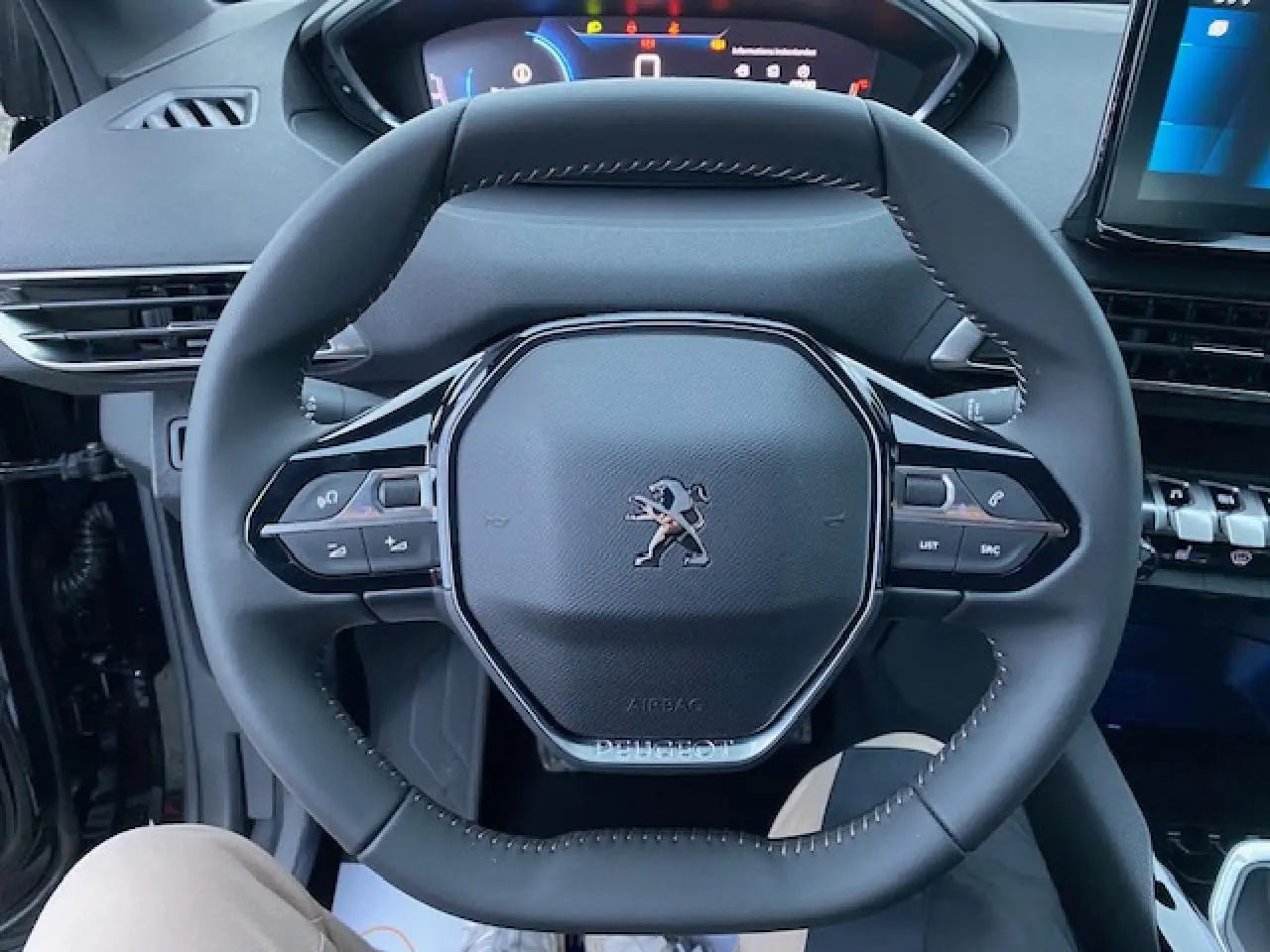 Vue rapprochée du volant noir du Peugeot 5008 2023 avec commandes intégrées et tableau de bord numérique en arrière-plan.