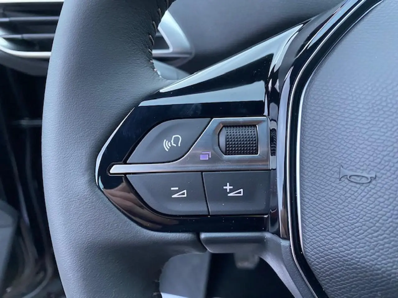Gros plan sur les commandes gauche du volant noir du Peugeot 5008 2023, avec boutons de volume et reconnaissance vocale.
