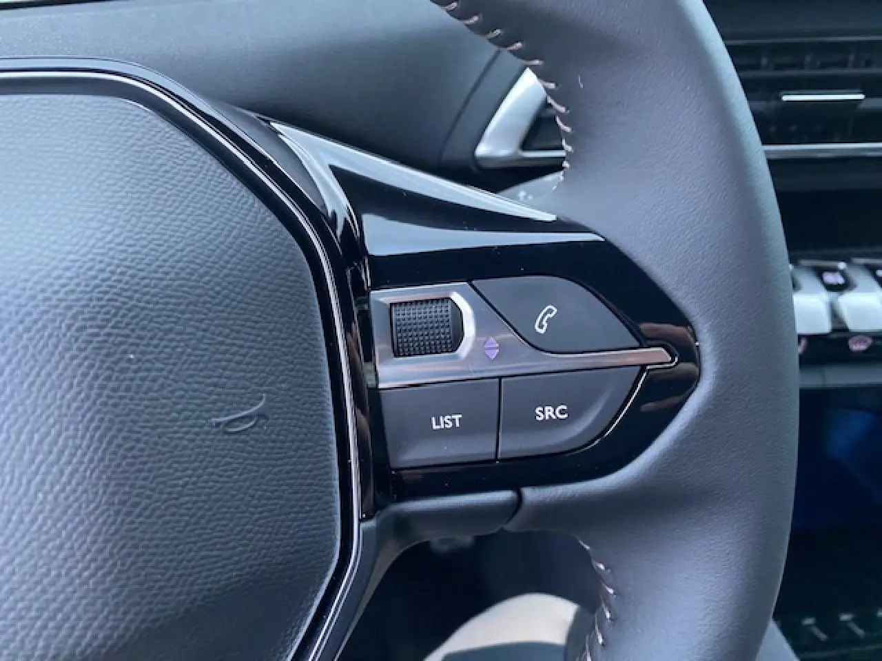 Gros plan sur les commandes gauche du volant noir du Peugeot 5008 2023 avec boutons de gestion audio et appel.