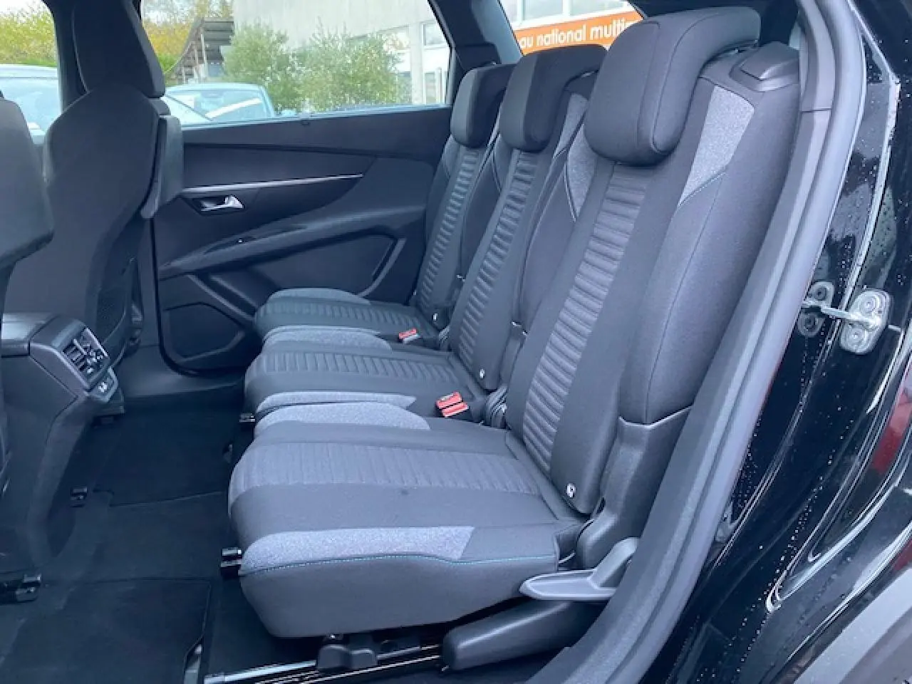 Vue latérale intérieure des sièges arrière noirs du Peugeot 5008 2023, avec portes ouvertes et habillage sombre.