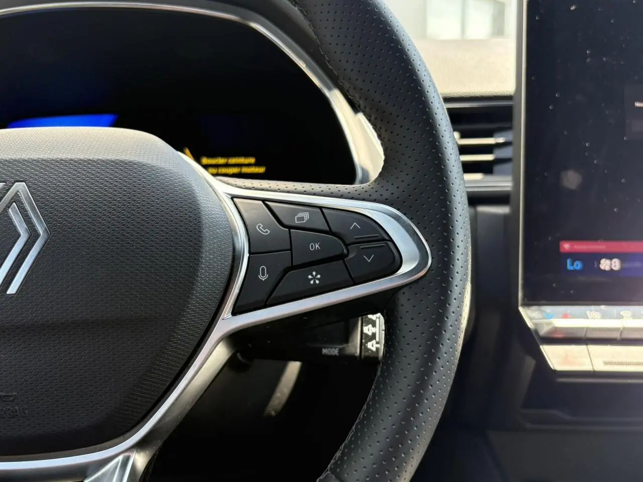 Gros plan sur le côté droit du volant perforé noir avec commandes intégrées et écran tactile du tableau de bord Renault Symbioz.