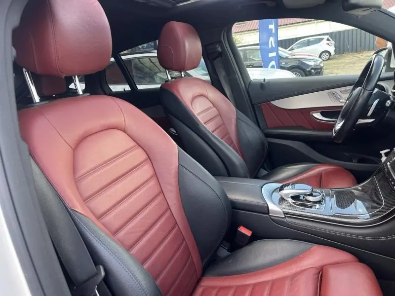 Vue intérieure côté conducteur du Mercedes GLC Coupé 220 d avec sièges sport cuir bicolore rouge et noir et console centrale en carbone.