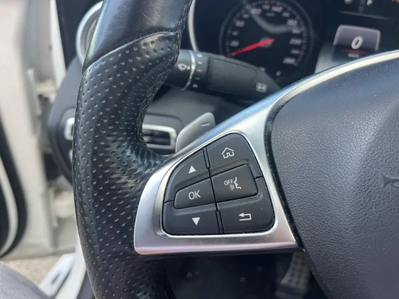Gros plan sur le côté gauche du volant cuir noir perforé du Mercedes GLC Coupé blanc diamant brillant, avec commandes multifonctions.