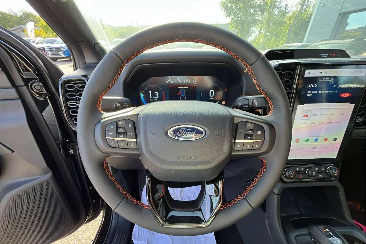 Vue intérieure centrée sur le volant cuir noir avec surpiqûres orange du Ford Ranger Wildtrak 2026, tableau de bord digital et écran tactile.