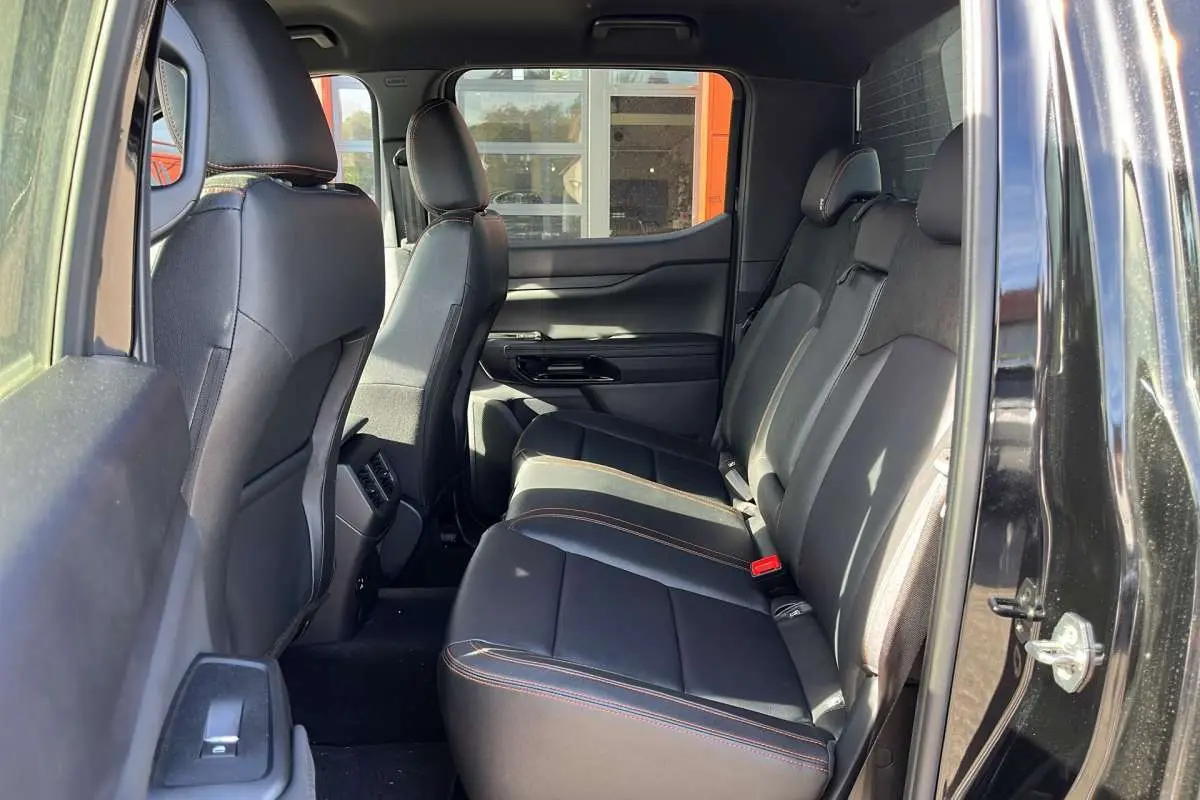 Vue intérieure côté droit sur la banquette arrière en cuir noir avec surpiqûres orange du Ford Ranger Wildtrak Plus noir agate.