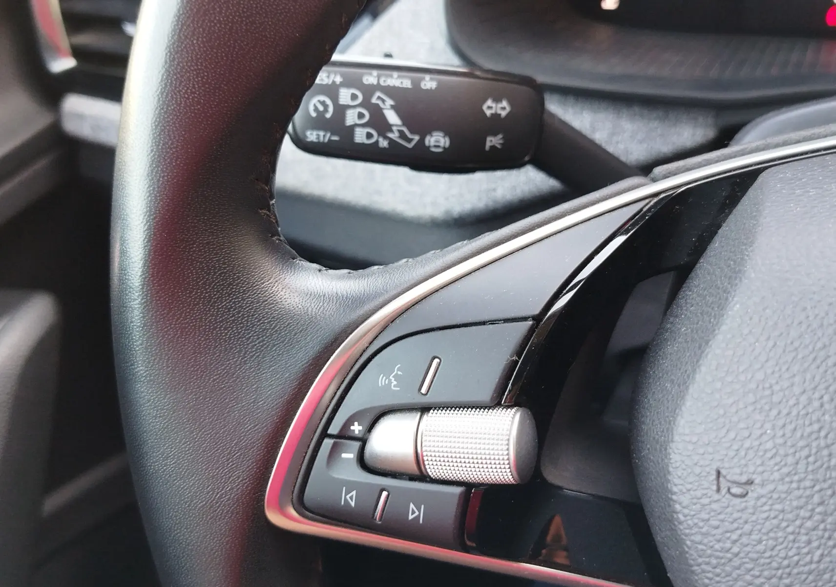 Gros plan sur les commandes gauche du volant noir du Skoda Kamiq 2024, avec molette argentée et boutons multifonctions.