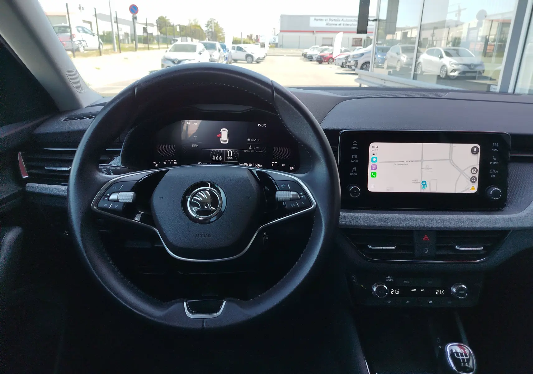 Vue intérieure centrée sur le volant et le tableau de bord numérique d'une Skoda Kamiq 2024, avec écran tactile et levier de vitesses manuel.