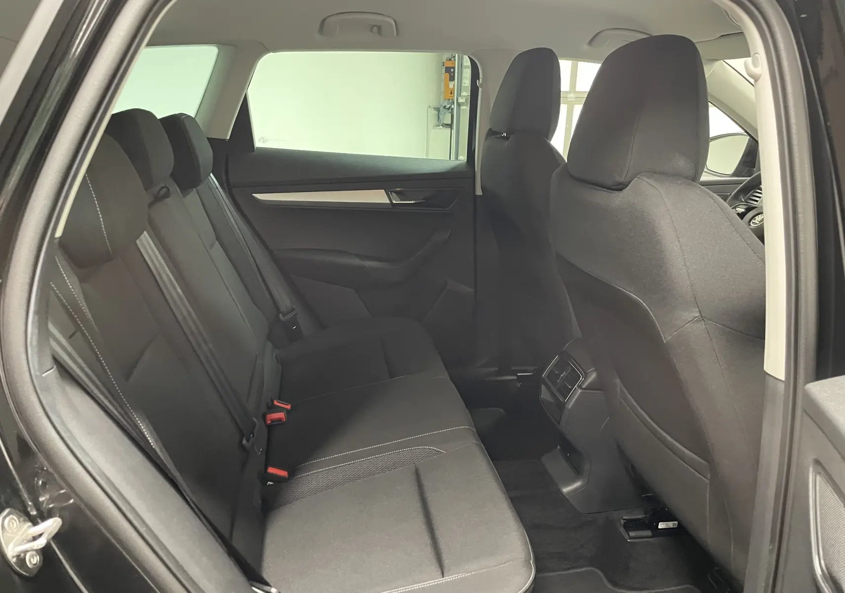 Vue intérieure du Skoda Karoq 2023 noir Magic nacré, montrant les sièges arrière côté gauche avec finitions sobres.