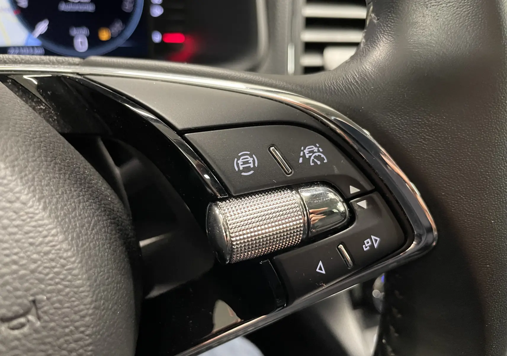 Gros plan sur les commandes au volant du Skoda Karoq 1.5 TSI noir nacré, avec molette métallique et boutons d'aide à la conduite.