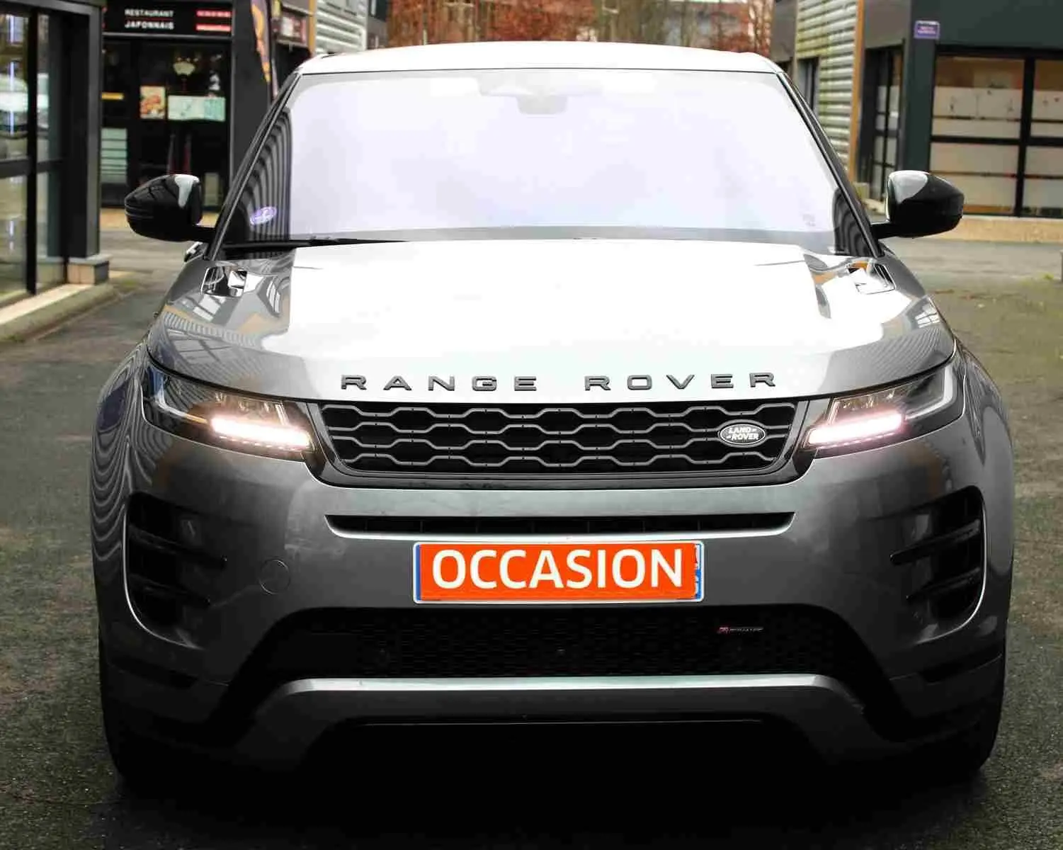 Vue frontale d'un Range Rover Evoque gris métal 2023 avec phares allumés et plaque "OCCASION" visible.