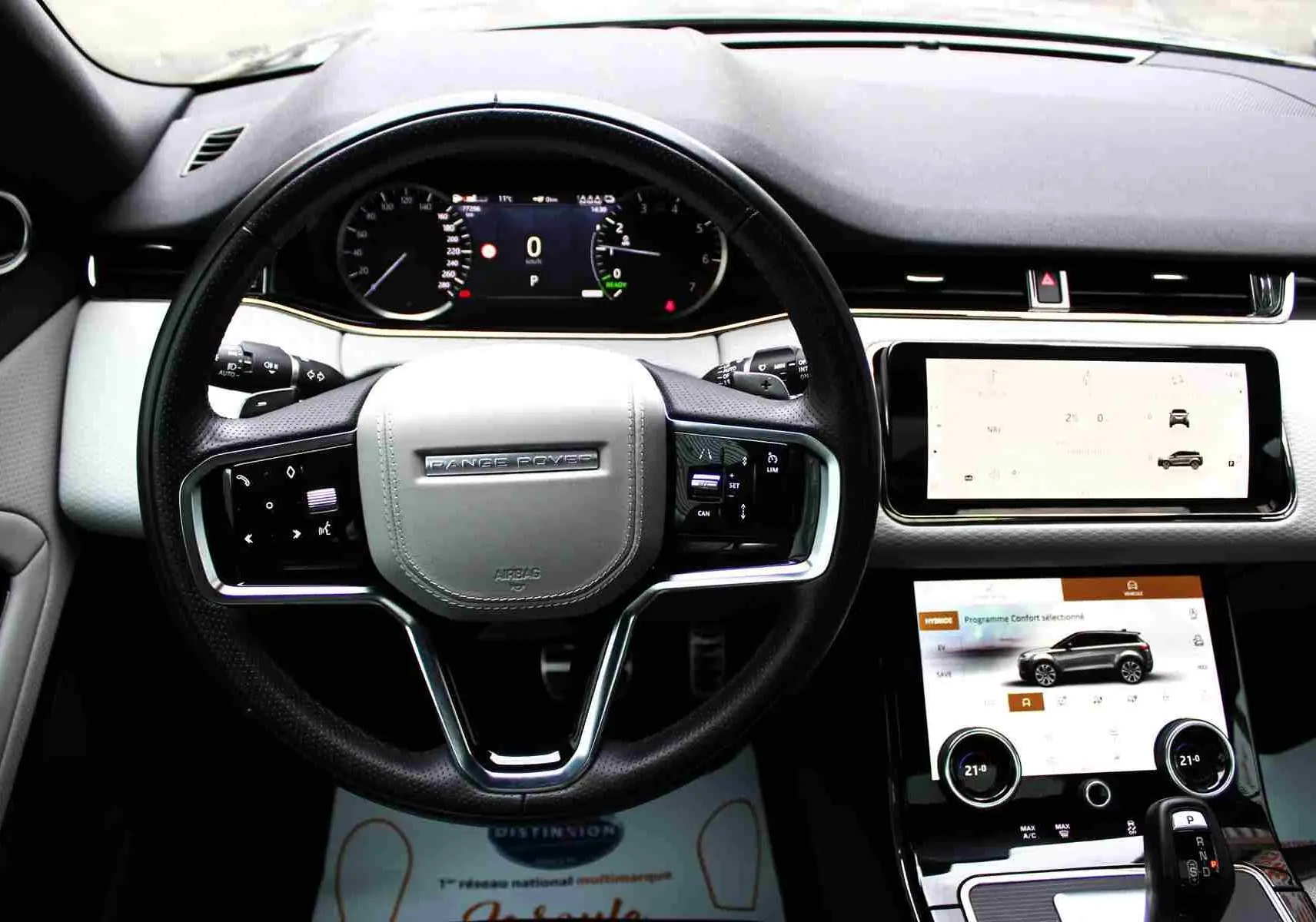 Vue intérieure centrée sur le volant gris clair et tableau de bord digital du Range Rover Evoque hybride rechargeable 2023.