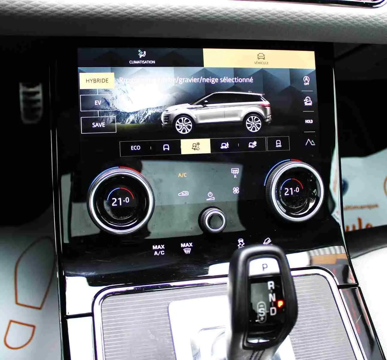 Vue rapprochée de la console centrale du Range Rover Evoque 2023 gris métal, affichant le mode hybride et la climatisation.