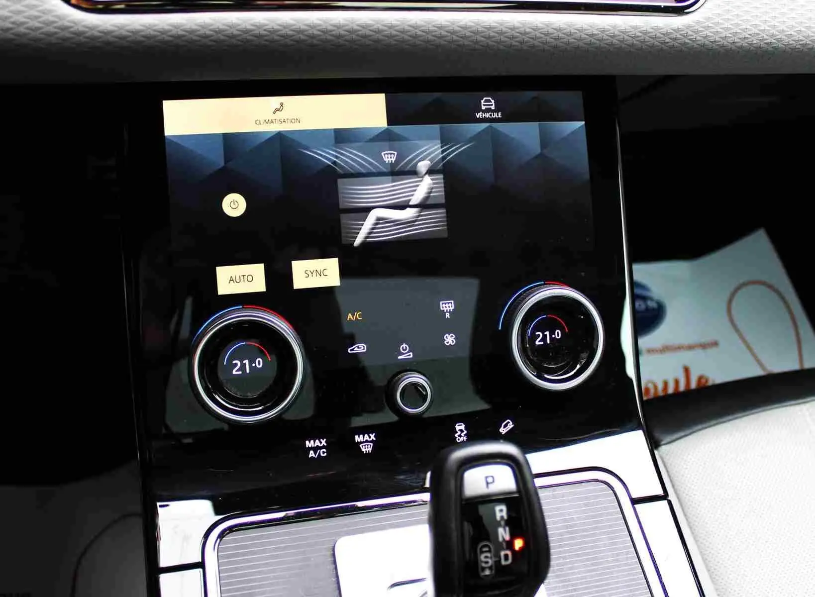 Gros plan sur la console centrale du Range Rover Evoque 2023 gris métal, affichant la climatisation digitale et le levier de vitesse.