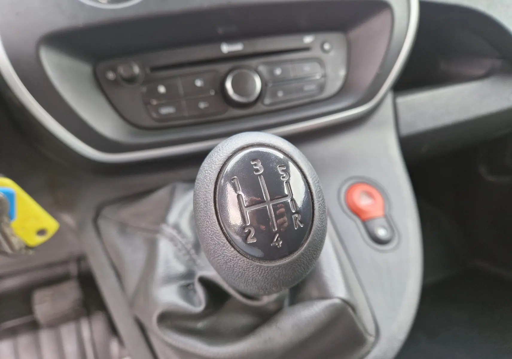 Gros plan sur le levier de vitesses manuel noir du Renault Kangoo blanc, avec console centrale et bouton de warning rouge visible.