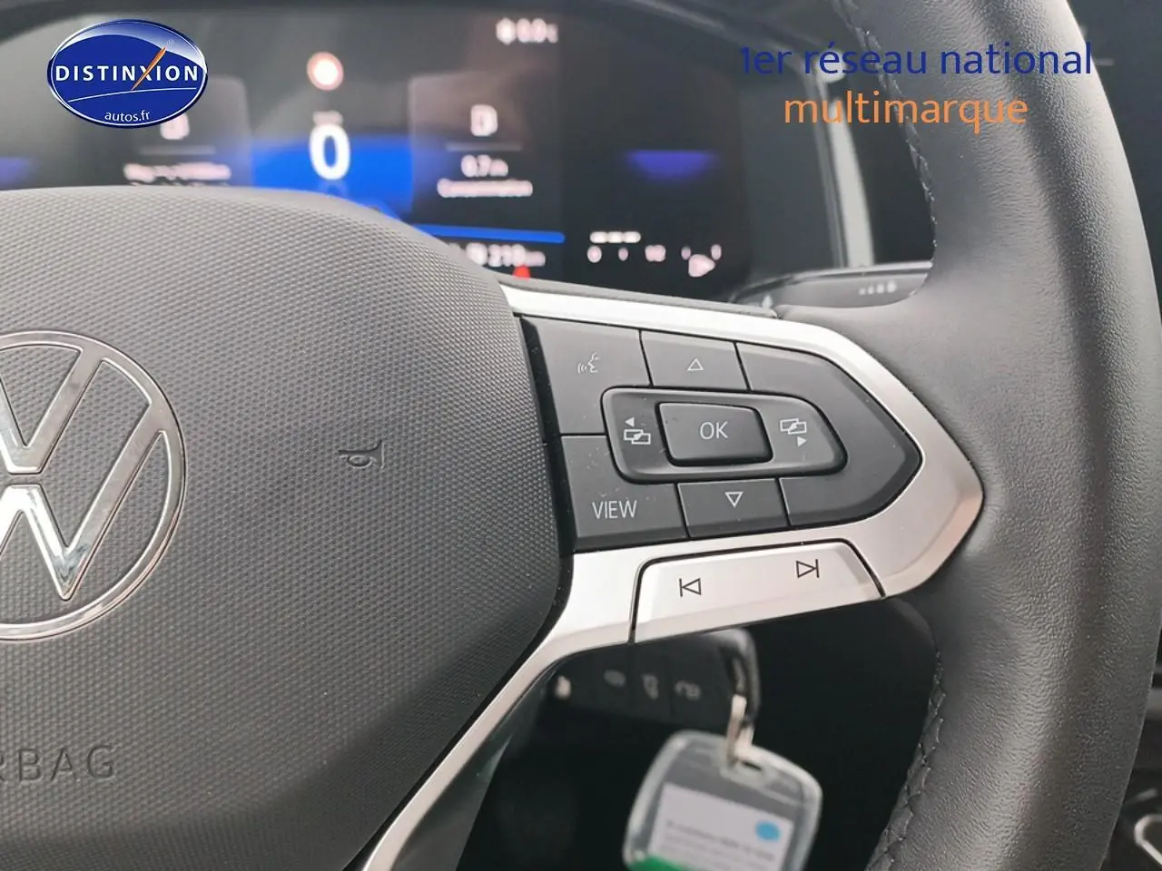 Gros plan sur le volant multifonction noir avec logo Volkswagen, tableau de bord digital flou en arrière-plan.