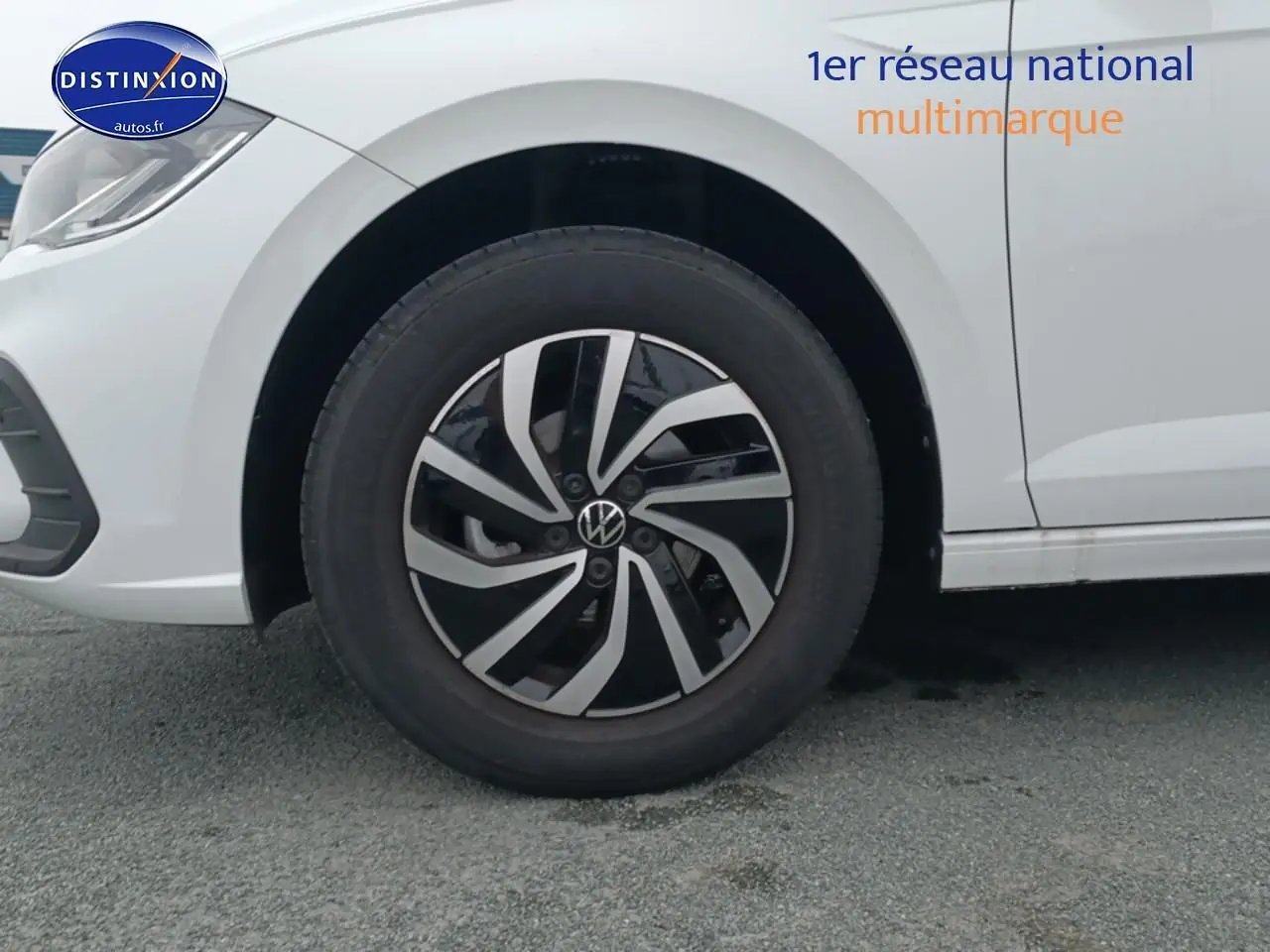 Gros plan sur la roue avant gauche et la jante alliage noire et argentée d'une Volkswagen Polo blanche.