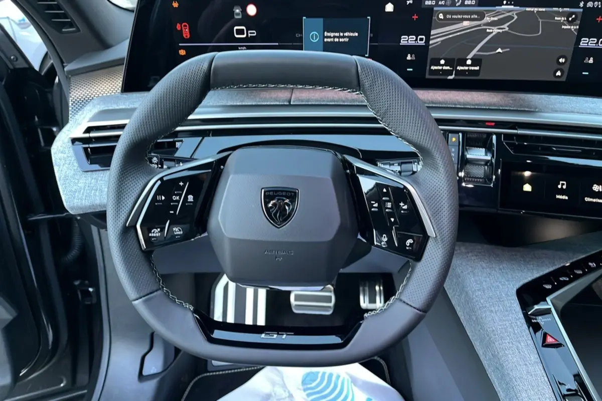 Vue rapprochée du volant cuir multifonctions Peugeot 5008 Hybrid GT avec tableau de bord numérique et finition Alcantara grise.