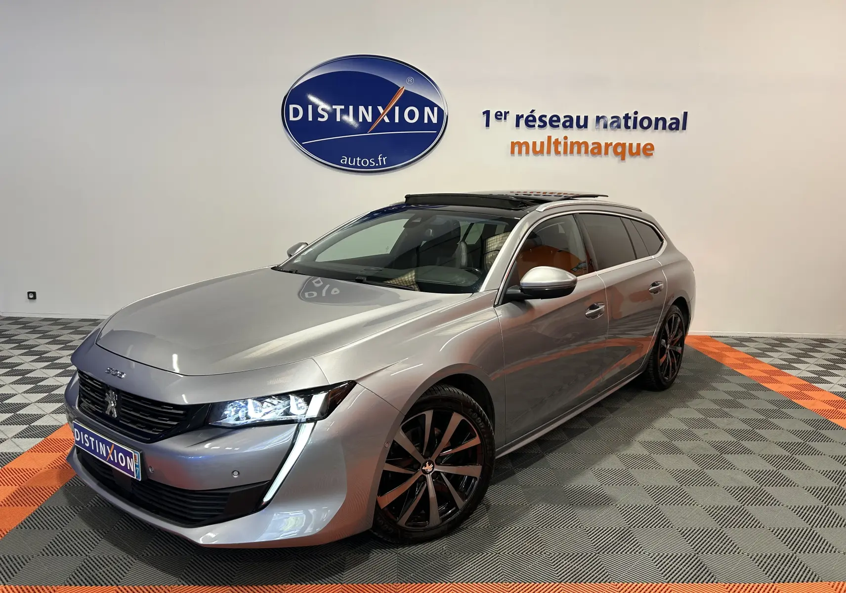 Peugeot 508 SW gris Platinium en 3/4 avant droit, avec toit ouvrant et jantes noires bicolores.