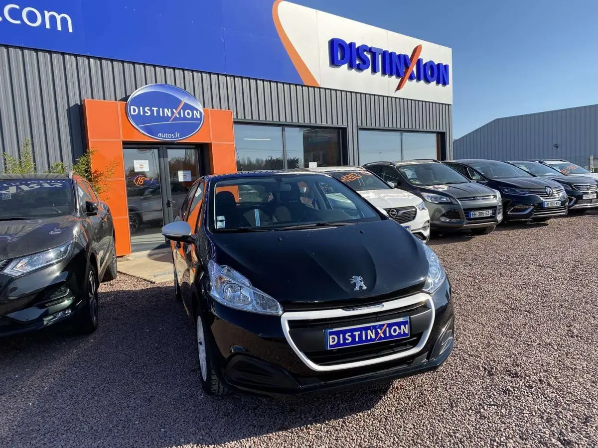 Peugeot 208 noire vue de face, avec jonc de calandre blanc, stationnée devant un concessionnaire Distinxion.