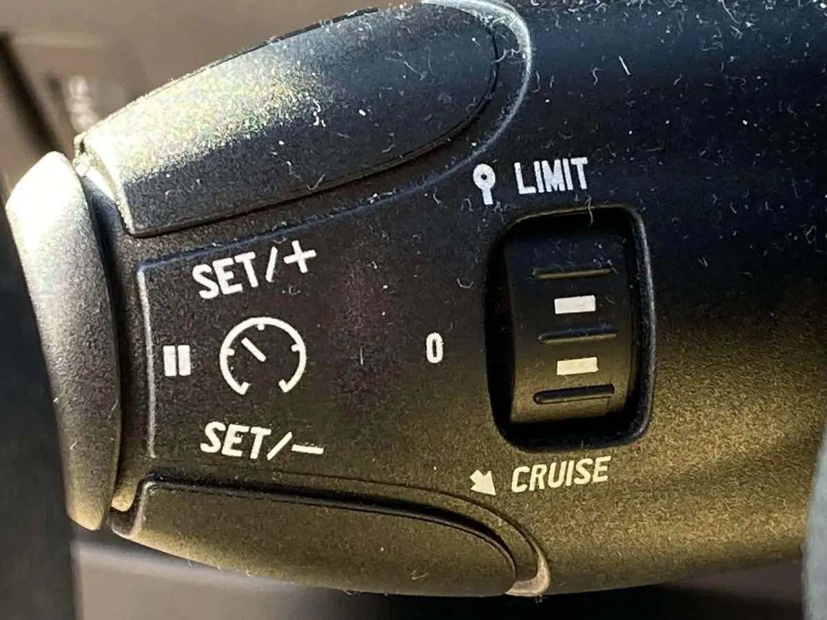 Gros plan sur la commande du régulateur et limiteur de vitesse de la Peugeot 208 noire de 2015.