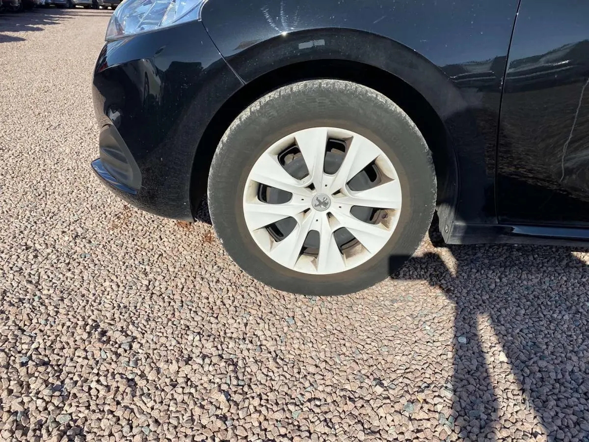 Gros plan sur la roue avant droite d'une Peugeot 208 noire, avec jante en acier et enjoliveur blanc.