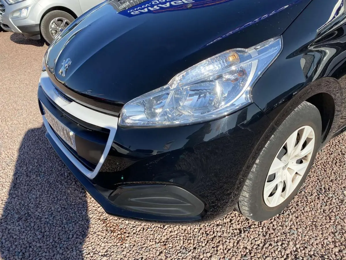 Vue 3/4 avant droit d'une Peugeot 208 noire avec jonc de calandre blanc et phare allumé.
