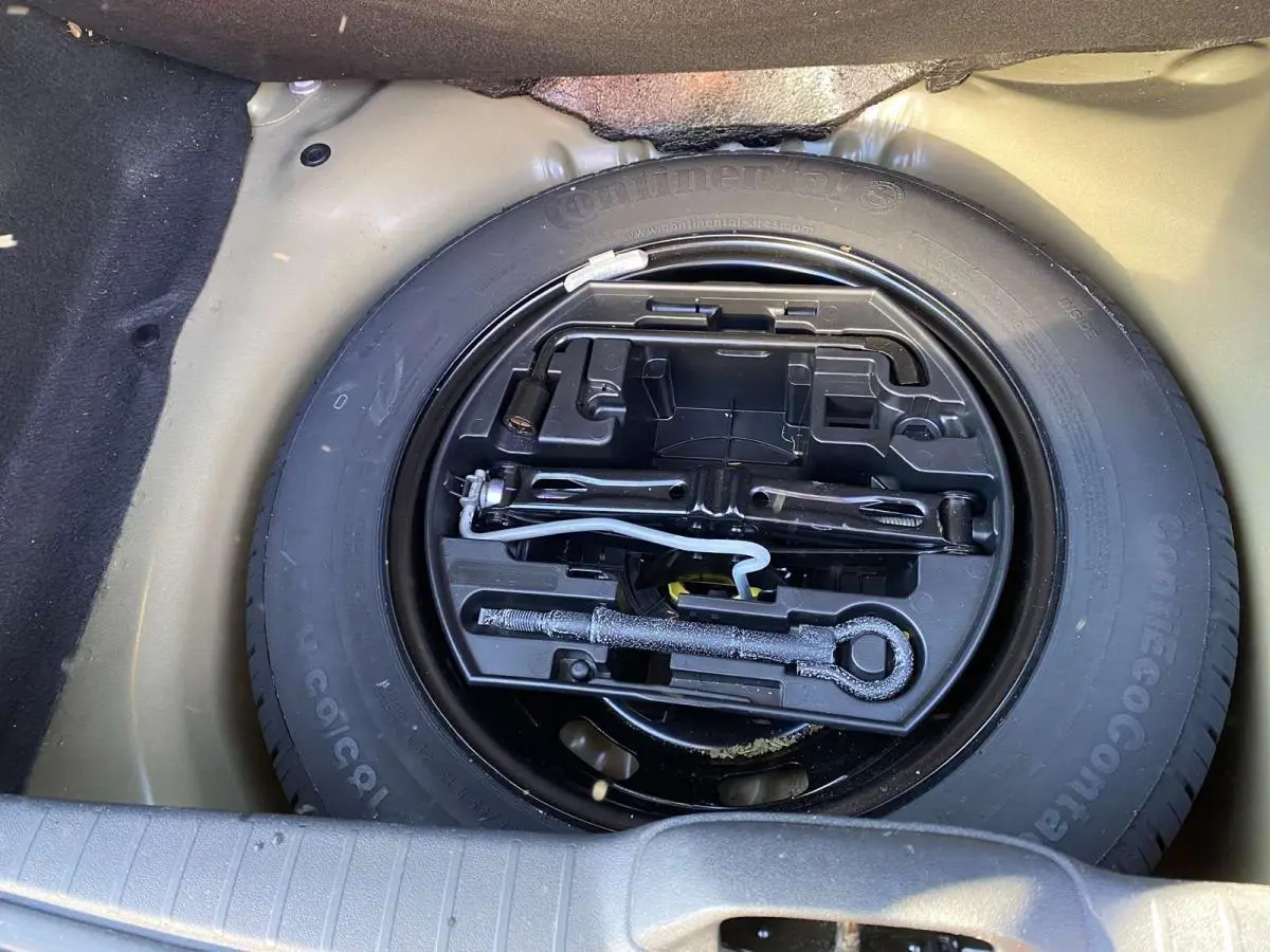 Gros plan sur la roue de secours acier 15 pouces noire avec kit d'outils dans le coffre d'une Peugeot 208 noire.