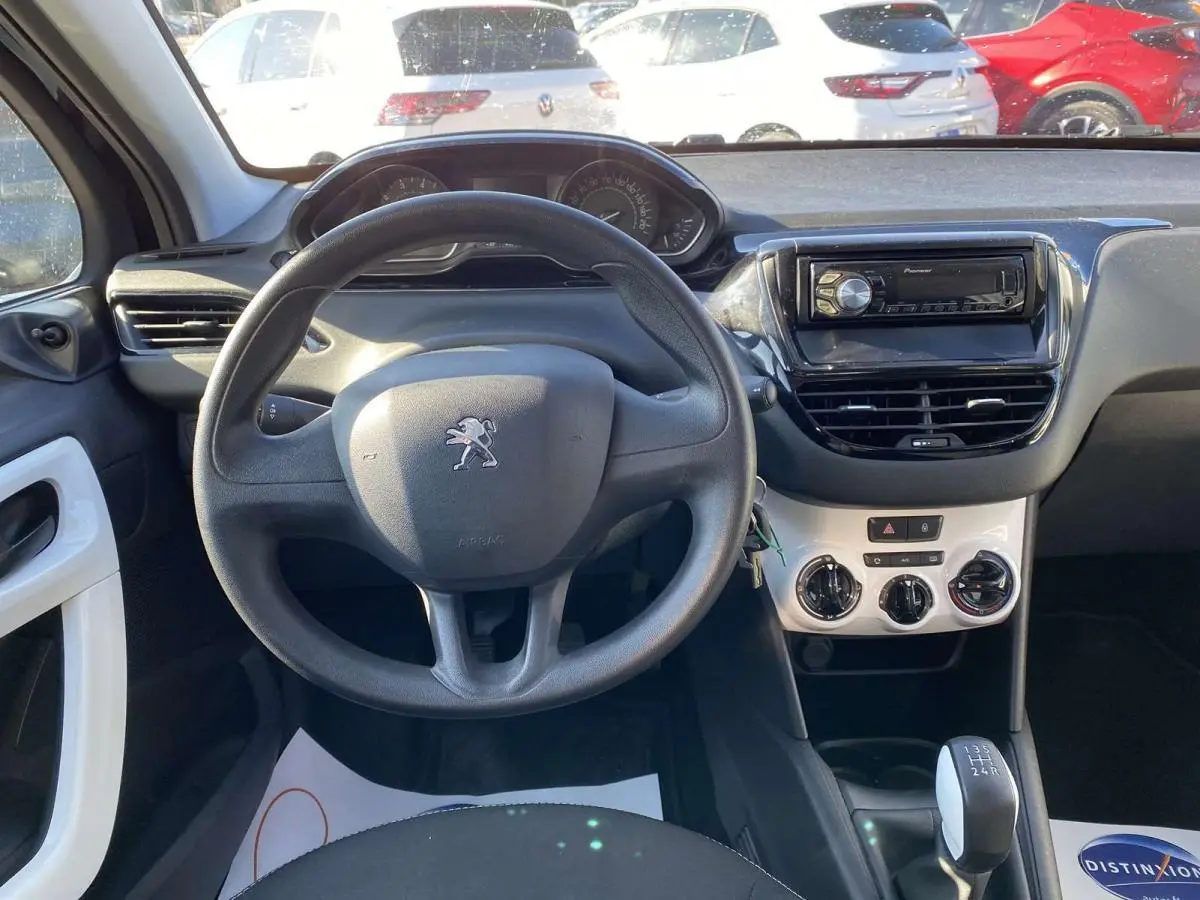 Vue intérieure centrée sur le volant Peugeot 208 noir, tableau de bord avec autoradio Pioneer et commande manuelle de vitesses.