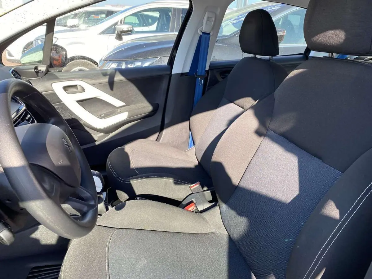 Vue intérieure côté conducteur de la Peugeot 208 noire, montrant les sièges avant et le volant au soleil.