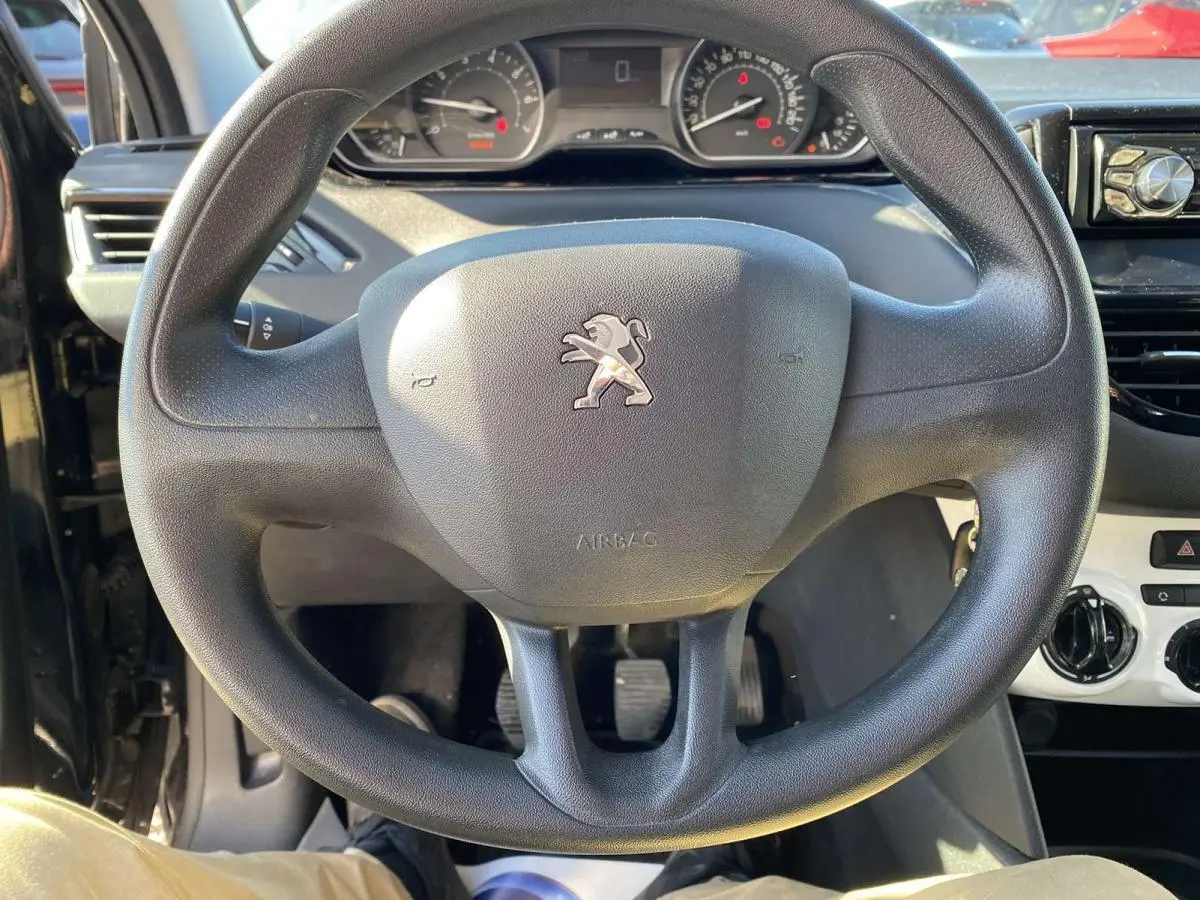 Vue rapprochée du volant noir de la Peugeot 208 2015 avec tableau de bord et commandes de climatisation visibles.