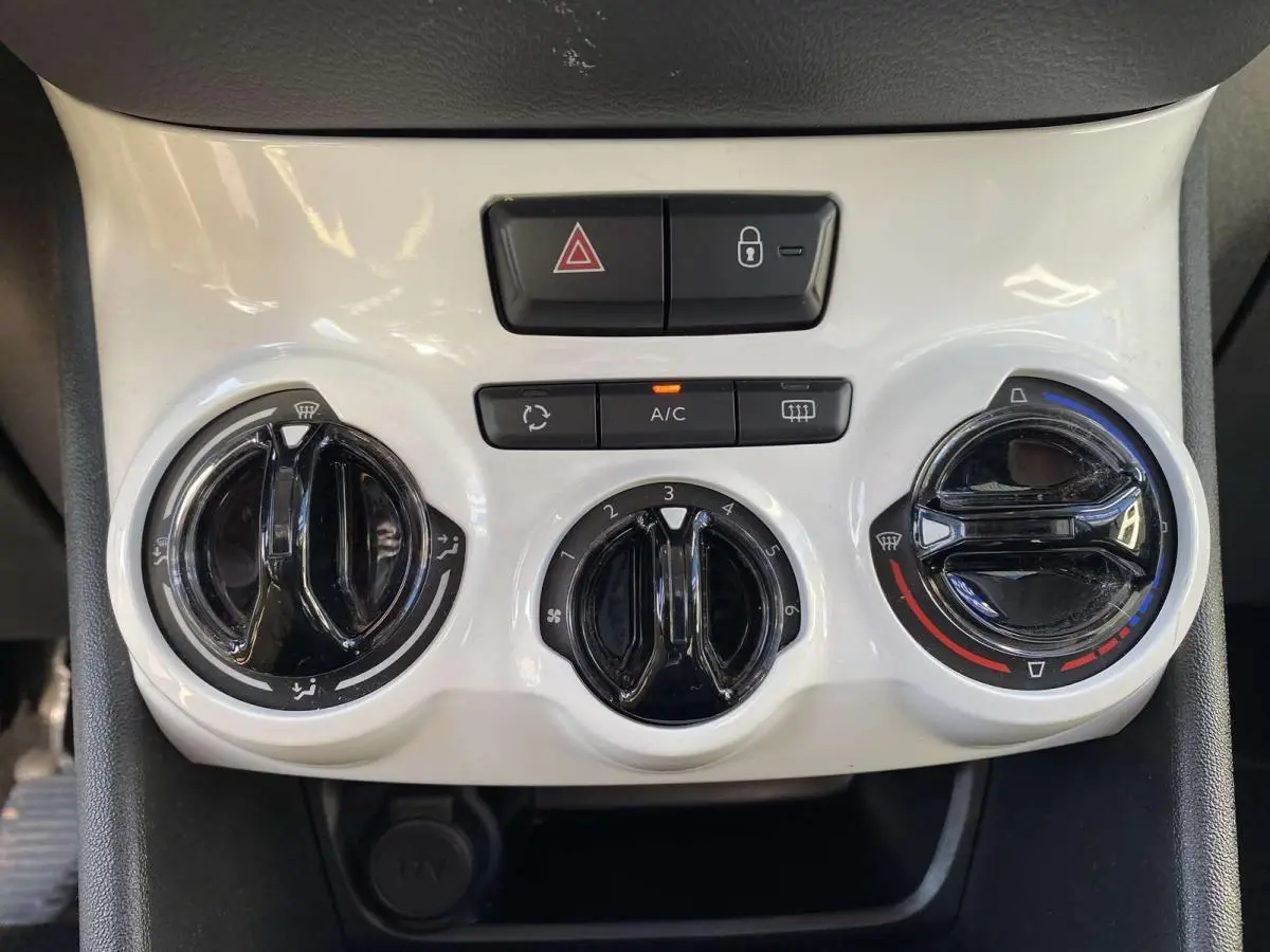 Vue rapprochée des commandes de climatisation et des boutons de sécurité sur la console centrale blanche d'une Peugeot 208 noire.