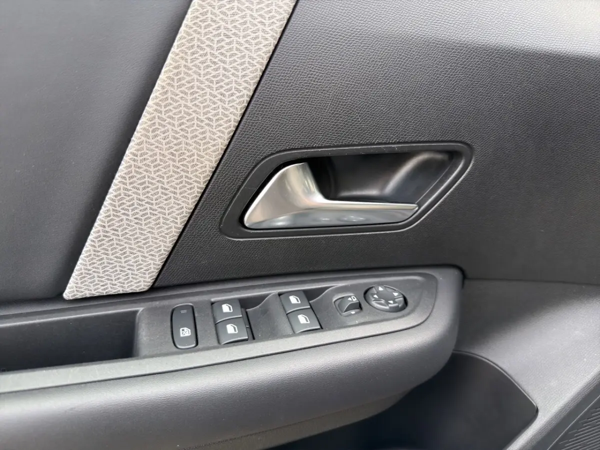 Gros plan sur la poignée intérieure et les commandes de fenêtre côté conducteur d'une Citroën C4 noire 2023.