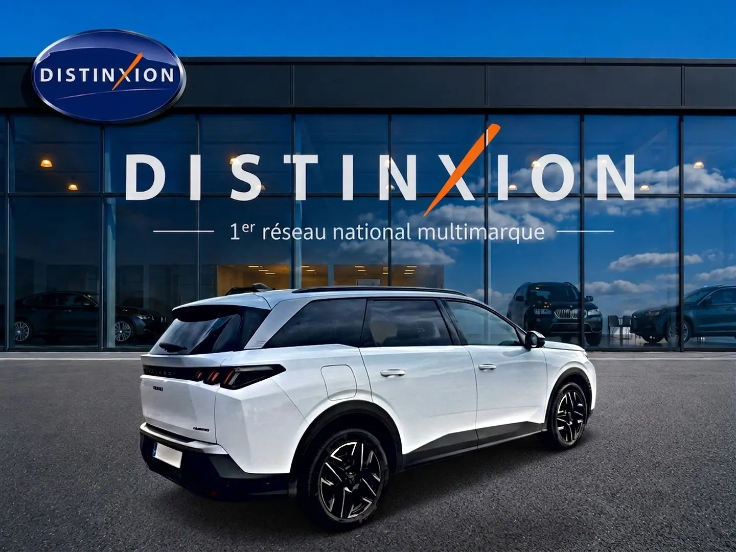 Peugeot 5008 Hybrid blanc en 3/4 arrière droit, avec toit noir et jantes alliage noires devant un showroom Distinxion.
