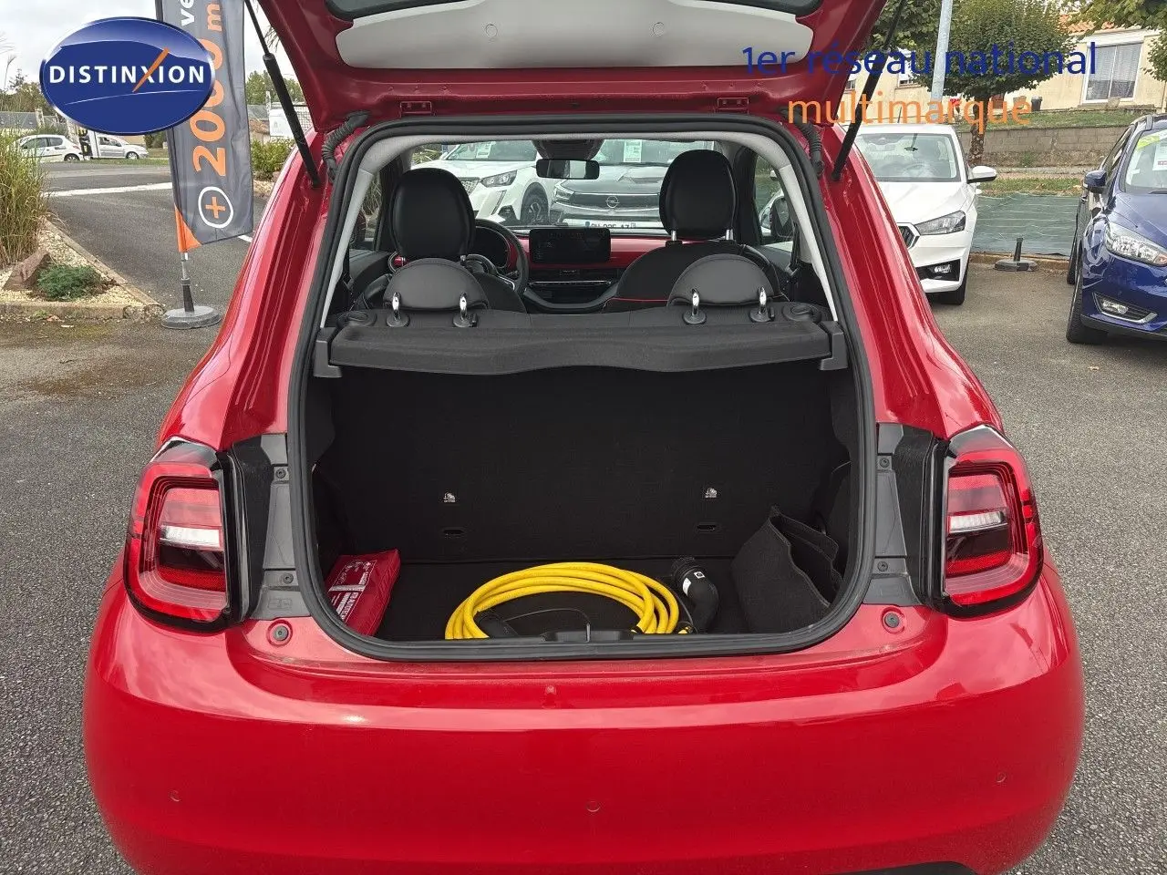 Vue arrière ouverte d'une FIAT 500e rouge 2024 montrant le coffre avec câble de recharge électrique rangé.