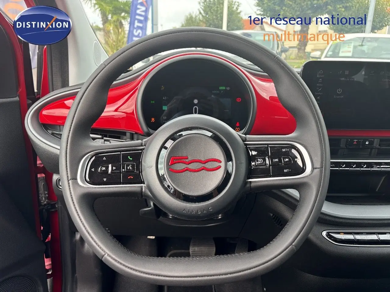 Vue intérieure centrée sur le volant noir avec logo rouge 500, tableau de bord et garniture rouge vif FIAT 500e 2024.