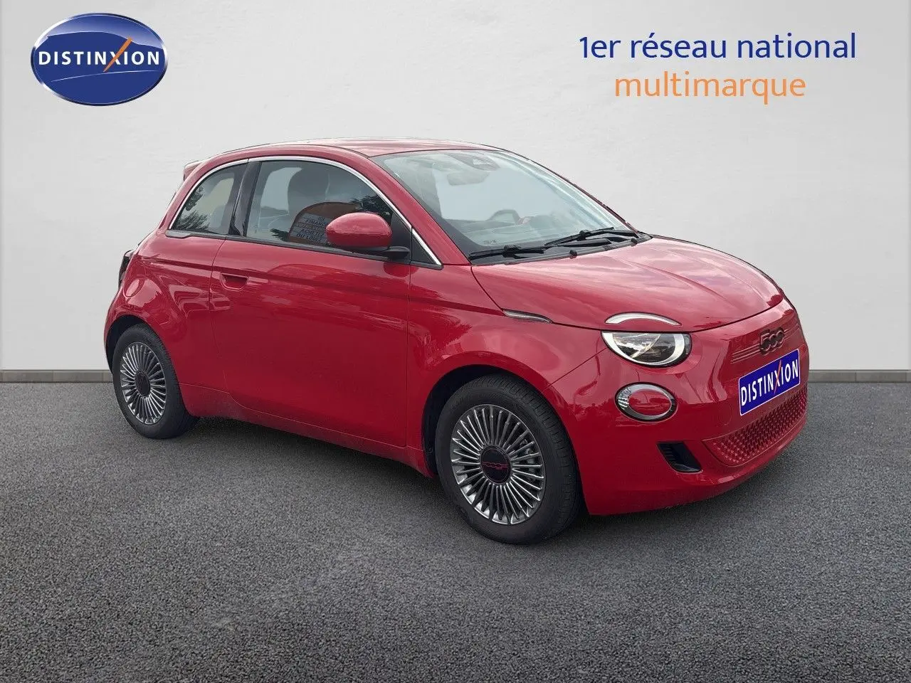 Fiat 500e rouge vue 3/4 avant droit, jantes classiques 15 pouces et phares ronds distinctifs.