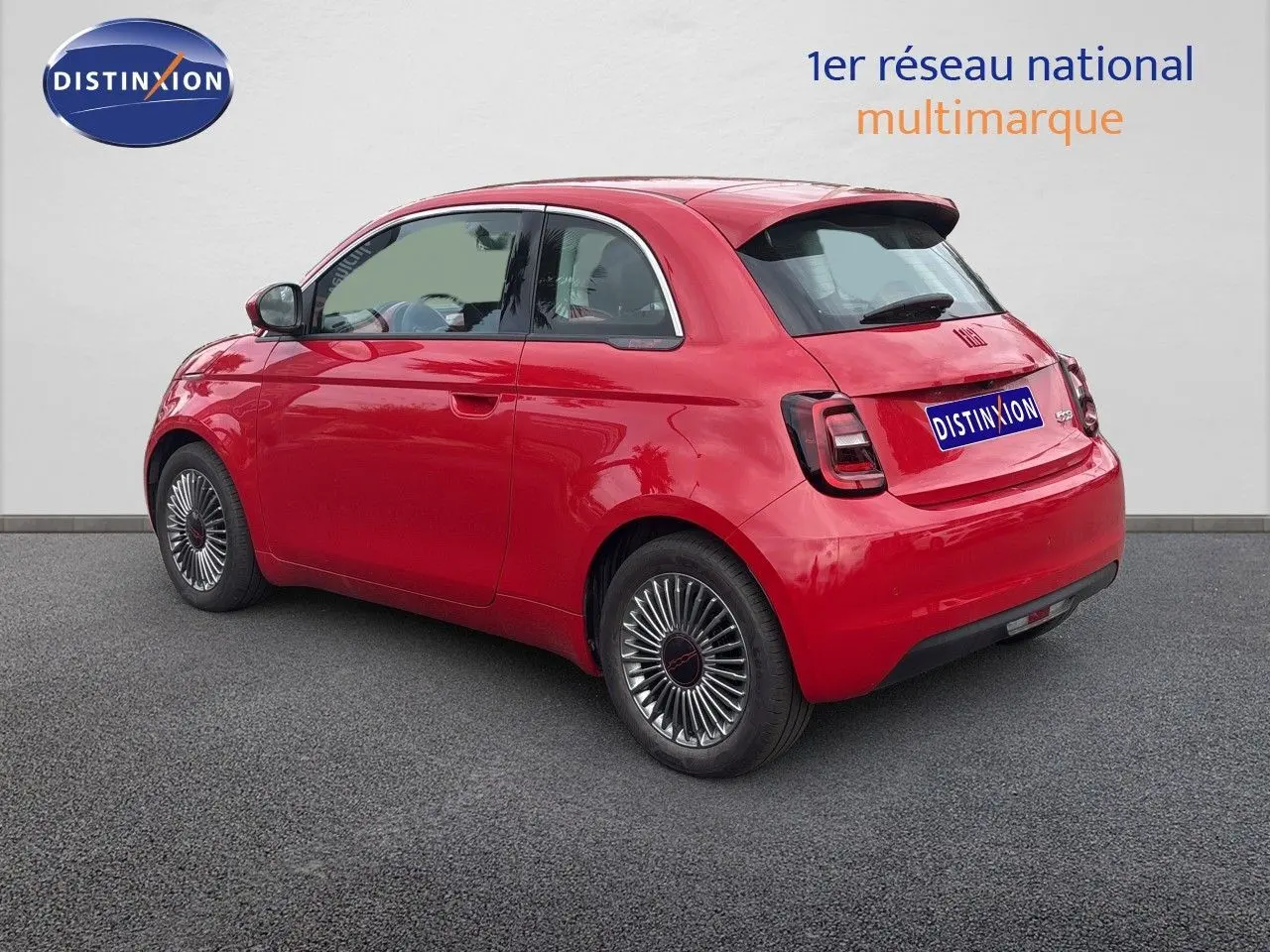 Vue 3/4 arrière droite d'une FIAT 500e rouge électrique 2024 avec jantes classiques et feux arrière sombres.