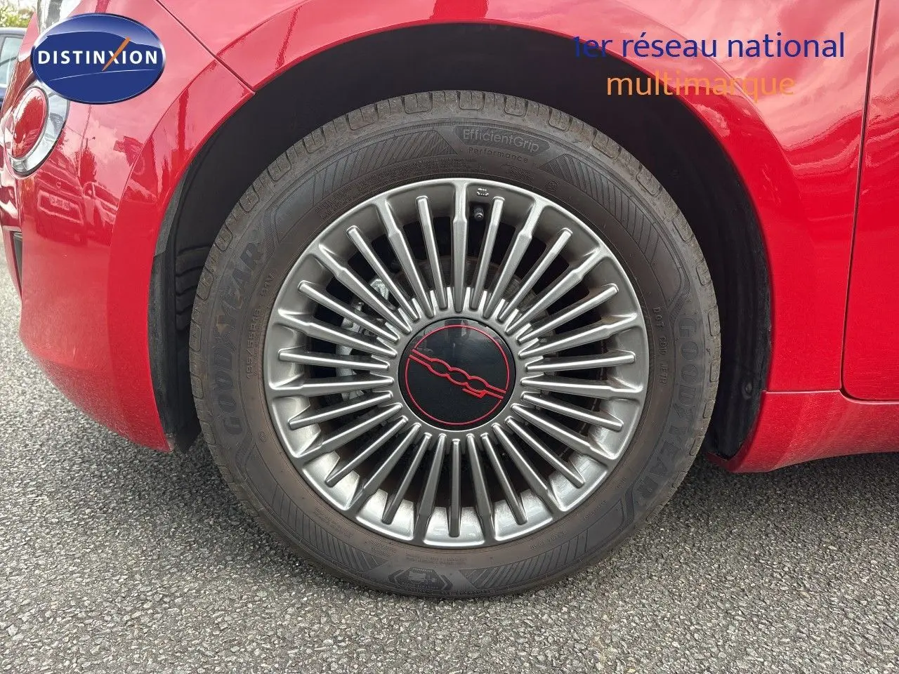 Gros plan sur la roue avant gauche d'une FIAT 500e rouge 2024 avec jante classique 15 pouces et logo central rouge.