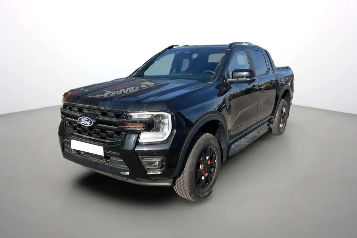Ford Ranger Wildtrak noir agate en 3/4 avant droit, avec jantes noires et détails orange sur les roues.