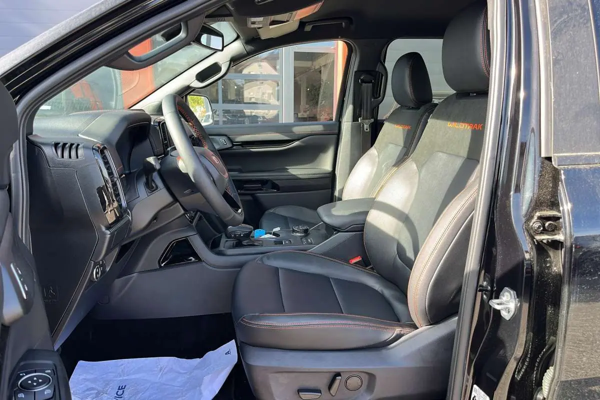 Vue intérieure côté conducteur du Ford Ranger Wildtrak 2026 noir agate, sièges cuir avec surpiqûres orange et console centrale visible.